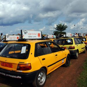 Des taxis urbain portant une plaque publicitaire demandant de vibrer football, garés à l'entrée du stade Amadou Ahidjo de Yaopundé.